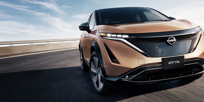 A Nissan Ariya running on the road between mountains front view