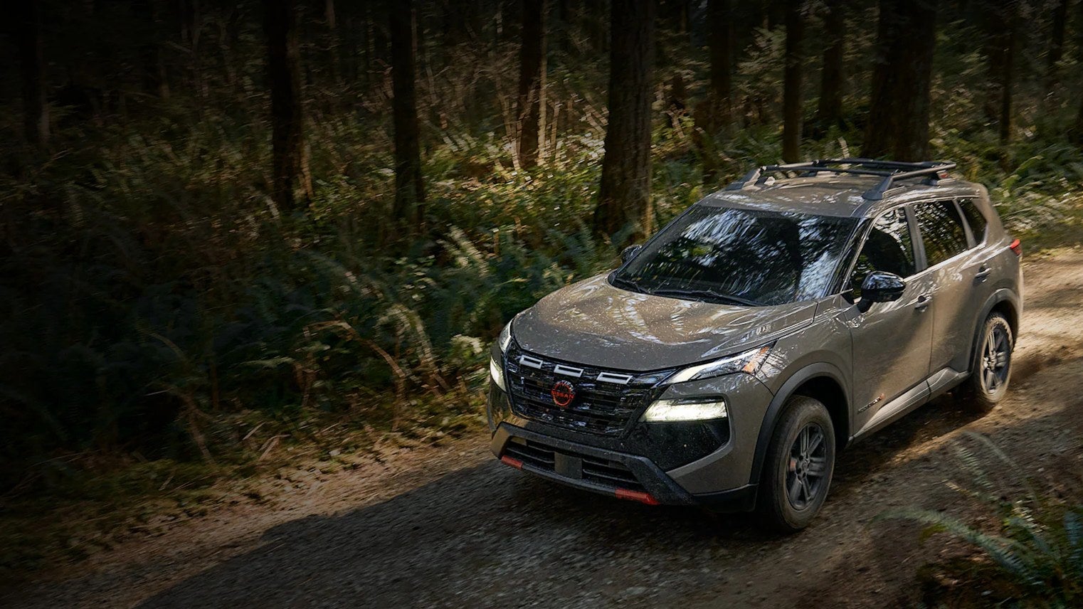 Gray Nissan Rogue crossover driving along a dirt trail through a forest