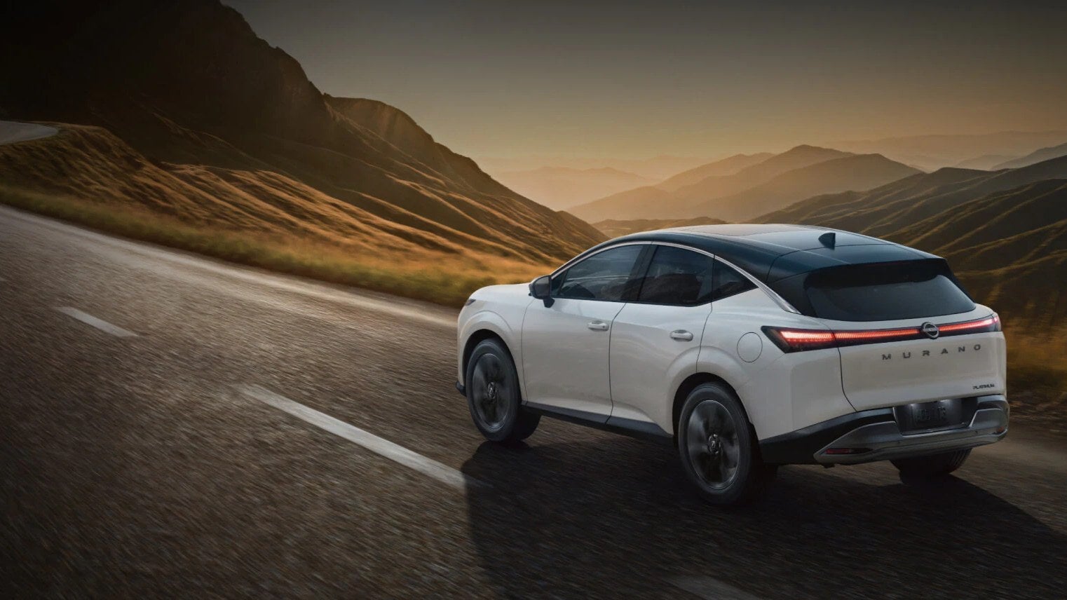 White Nissan Murano SUV driving along a winding road at sunset